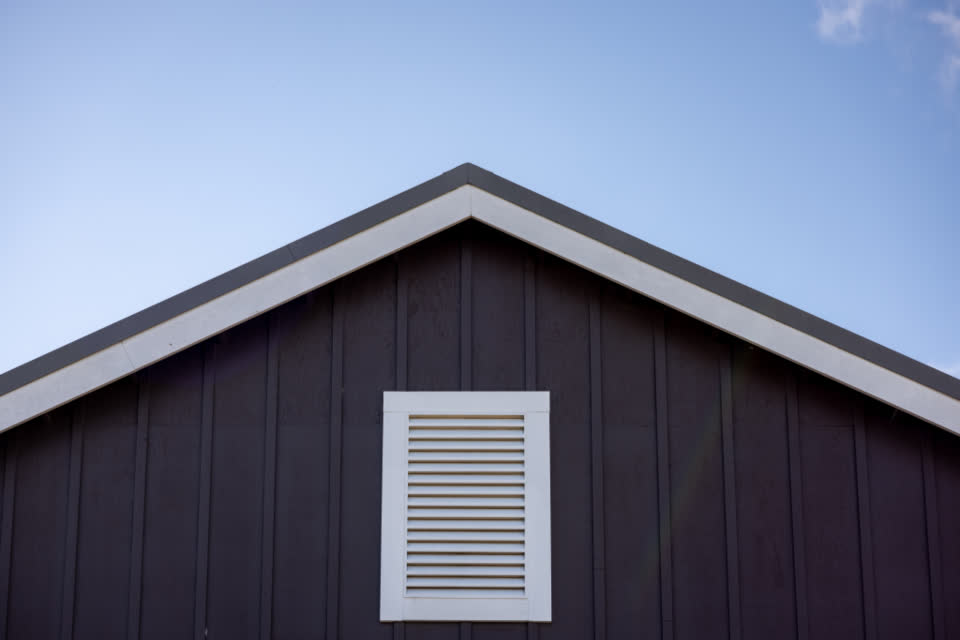 A dark timber gable with a single louvred vent under the roof ridge