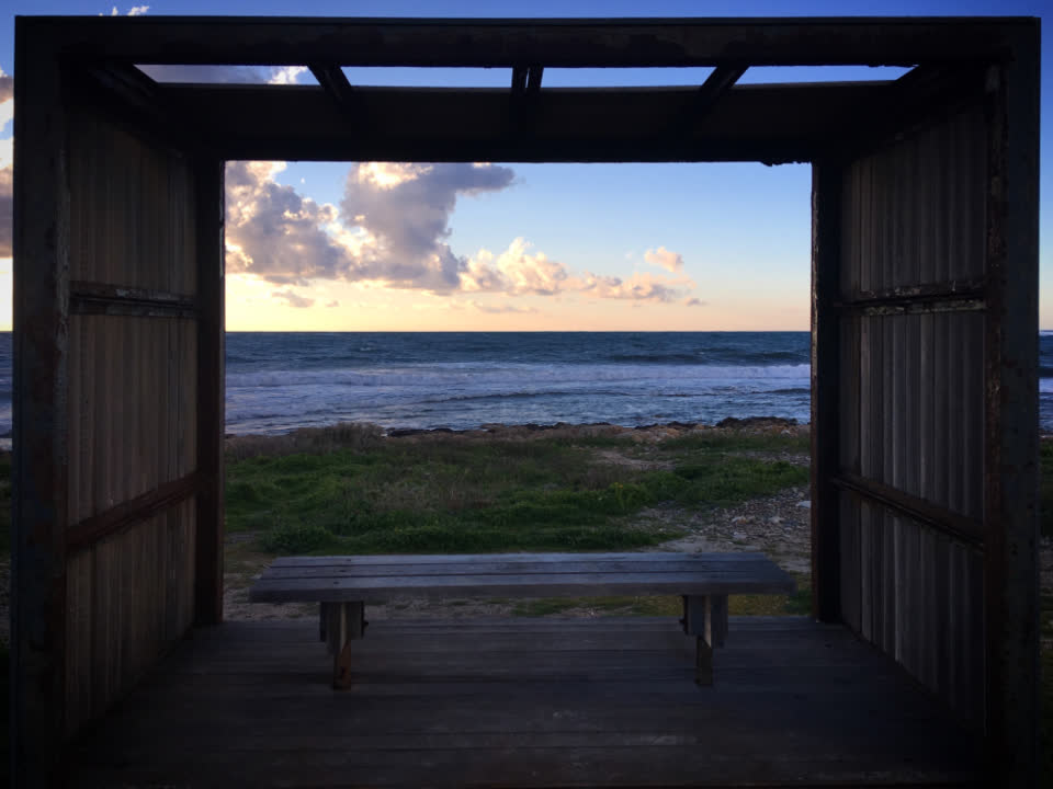A timber frame opening onto the sea, with a plain bench in the foreground